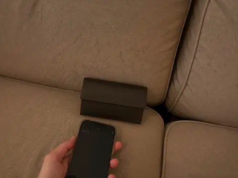 Cartera entre los cojines del sillón y un celular en la mano